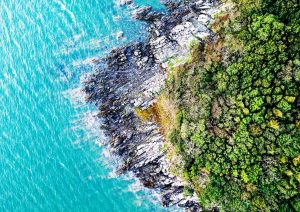 Top down aerial image showing a section of coastline with the sea to the right of the image. There is a rocky coastline leading to a wood on the right.