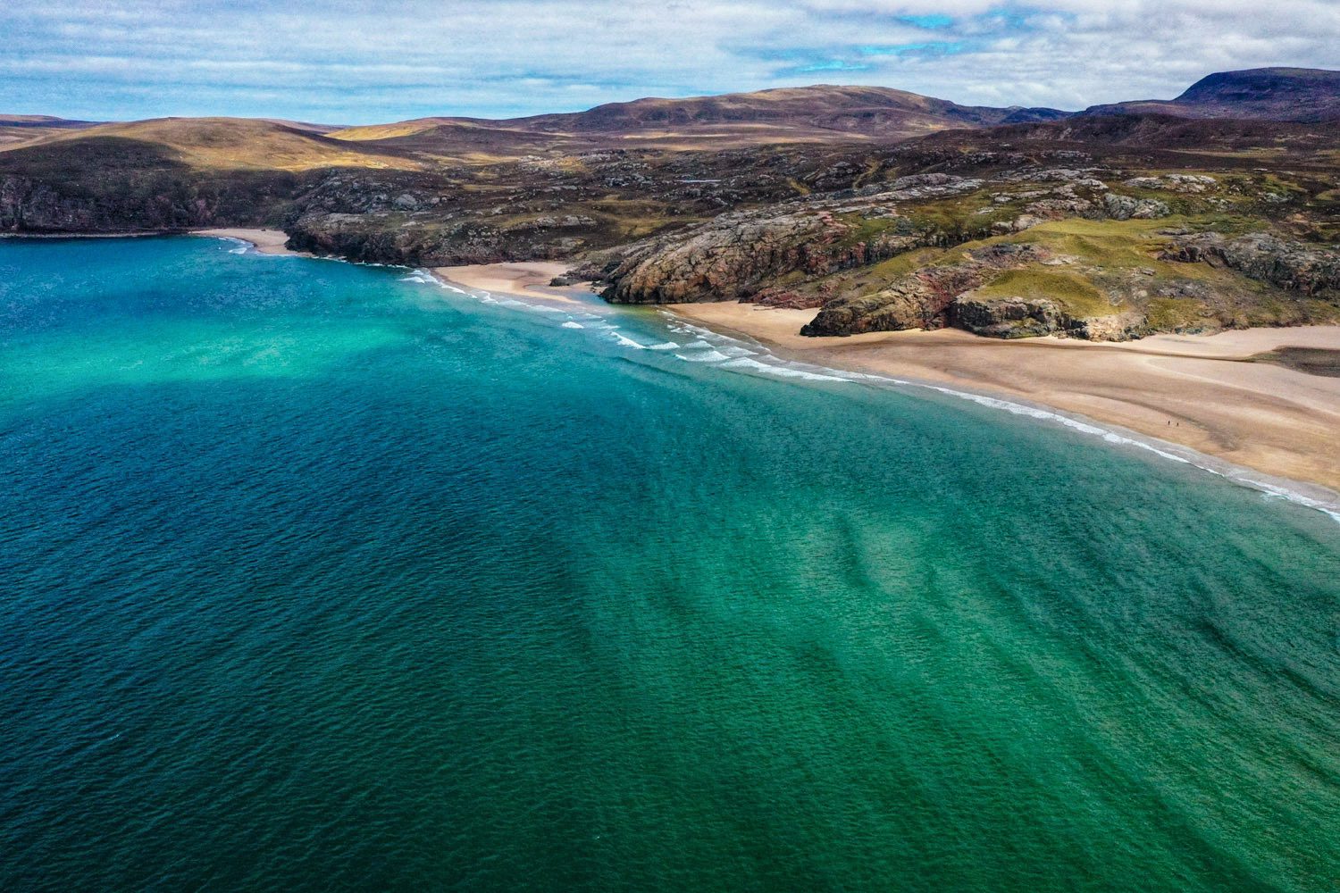 Drone photograph of the coastline of North West Scottish Highlands. The photograph shows and emerald coloured Atlantic Ocean next to a series of bays leading to a wild undeveloped landscape.
