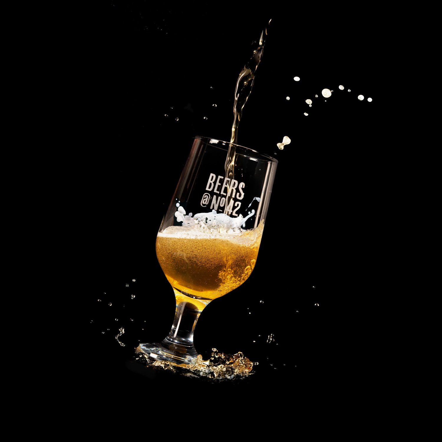product photography showing beer being poured into a beer glass against a black background. There are splashes of beer coming from the top of the glass.
