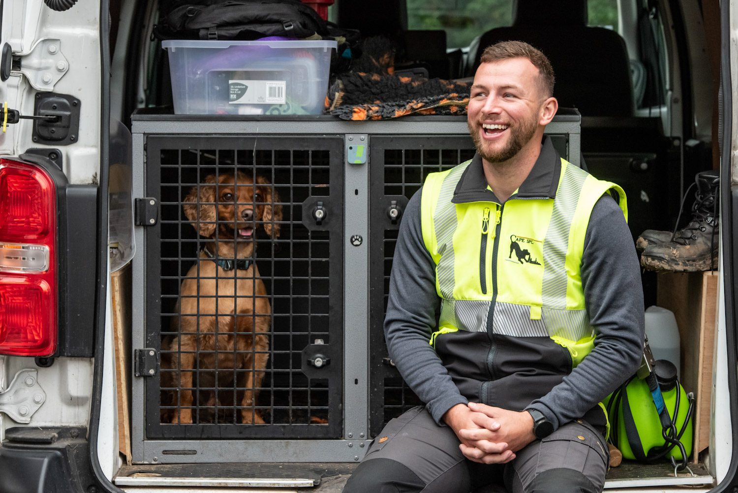 detection dog in van with handler sitting next to him